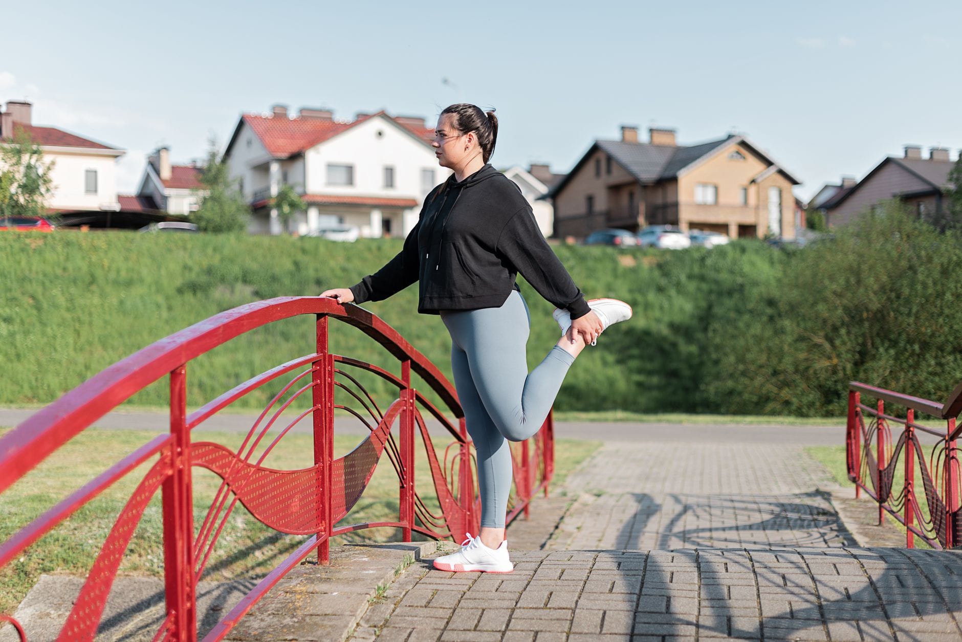 Kobieta w sportowym stroju rozciąga się na czerwonym moście w parku